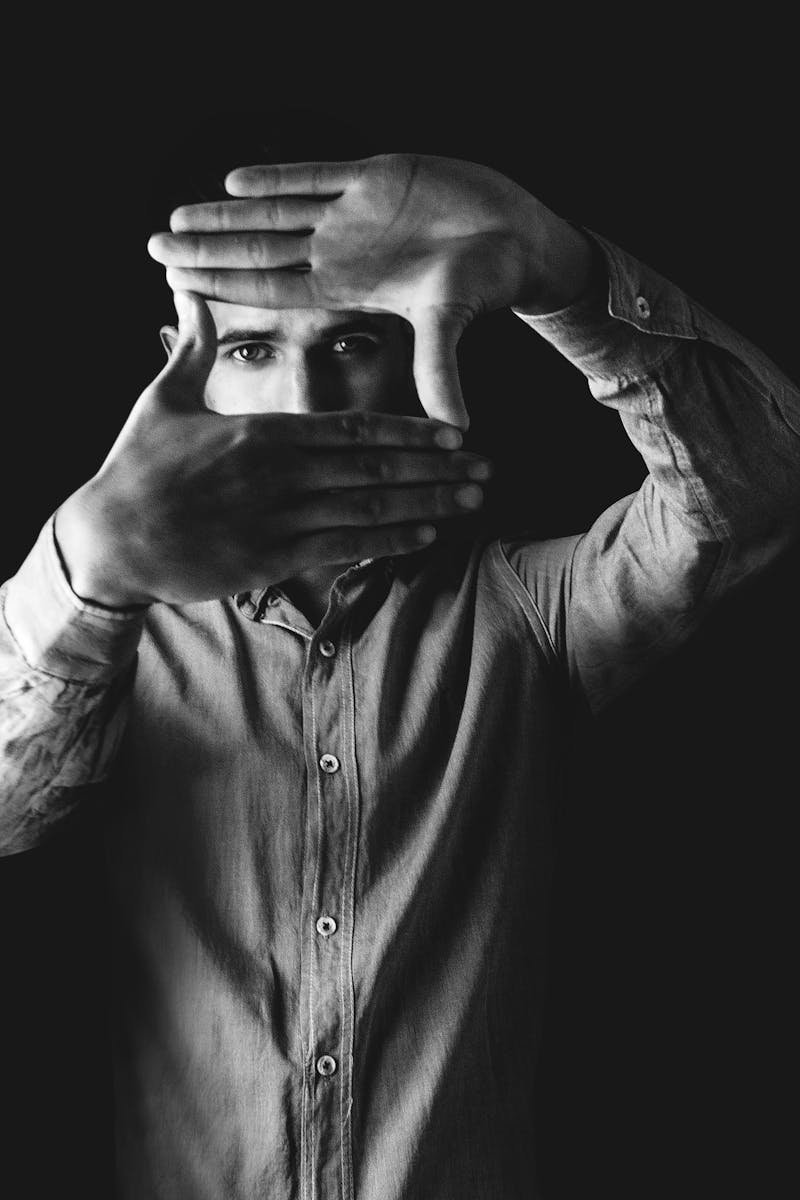 Black and white portrait of a man framing his face with his hands, creating an artistic, moody effect.